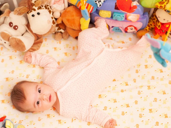 A baby girl in a crib with many toys