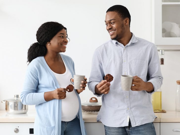 pregnant woman and husband eating cookie and drinking tea in the kitchen