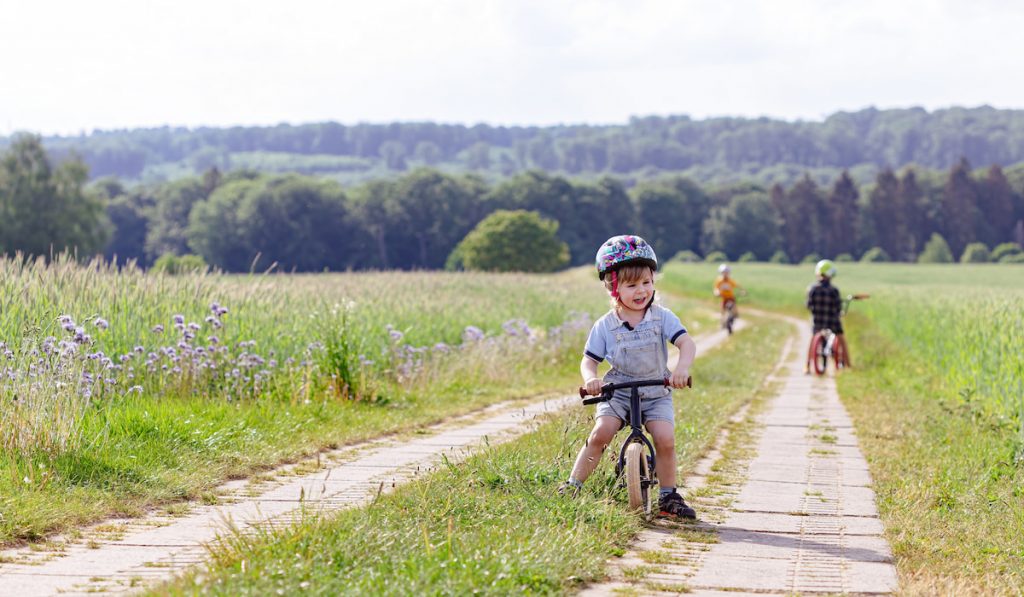 A boy in a helmet riding on a rural road on a balancing bike on a hot summer day
