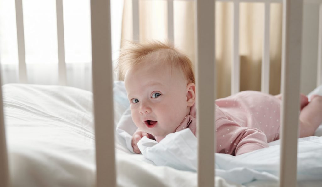 Awake baby girl looking at camera while creeping in crib
