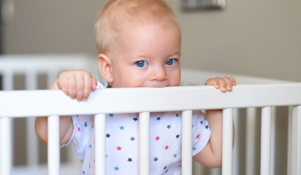 Baby boy standing in crib biting