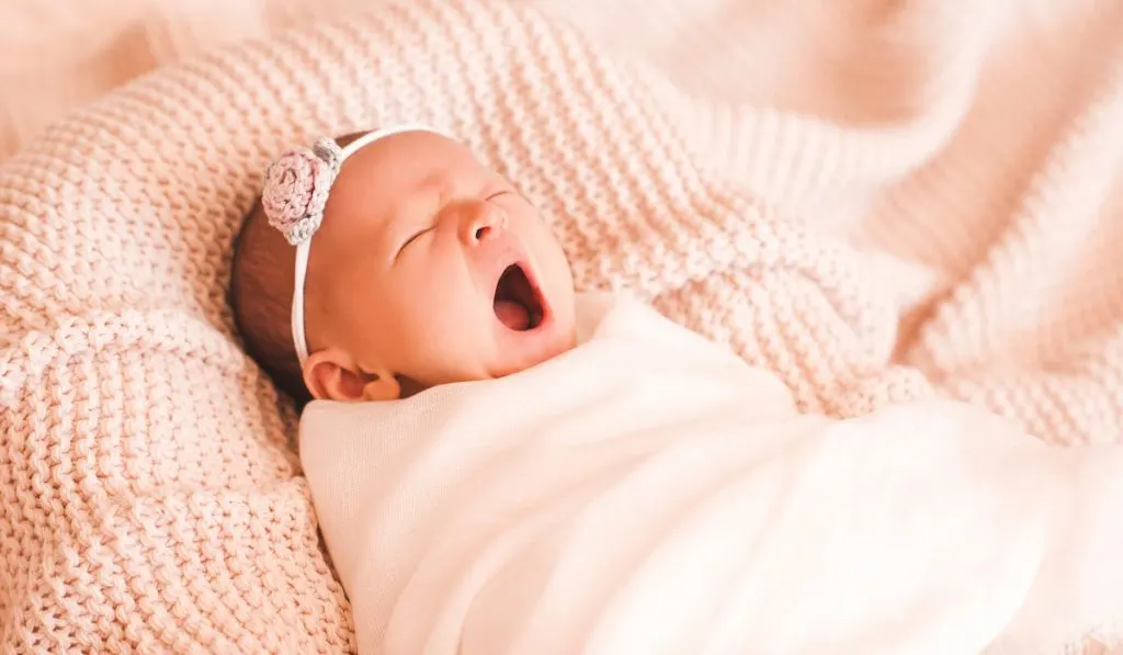 Baby girl yawning swaddled in bed closeup