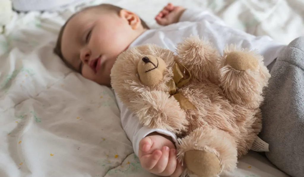 Baby sleeping in bed with teddy bear
