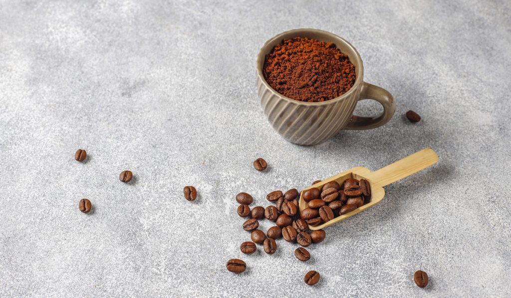 Coffee beans and coffee ground in a mug on gray background