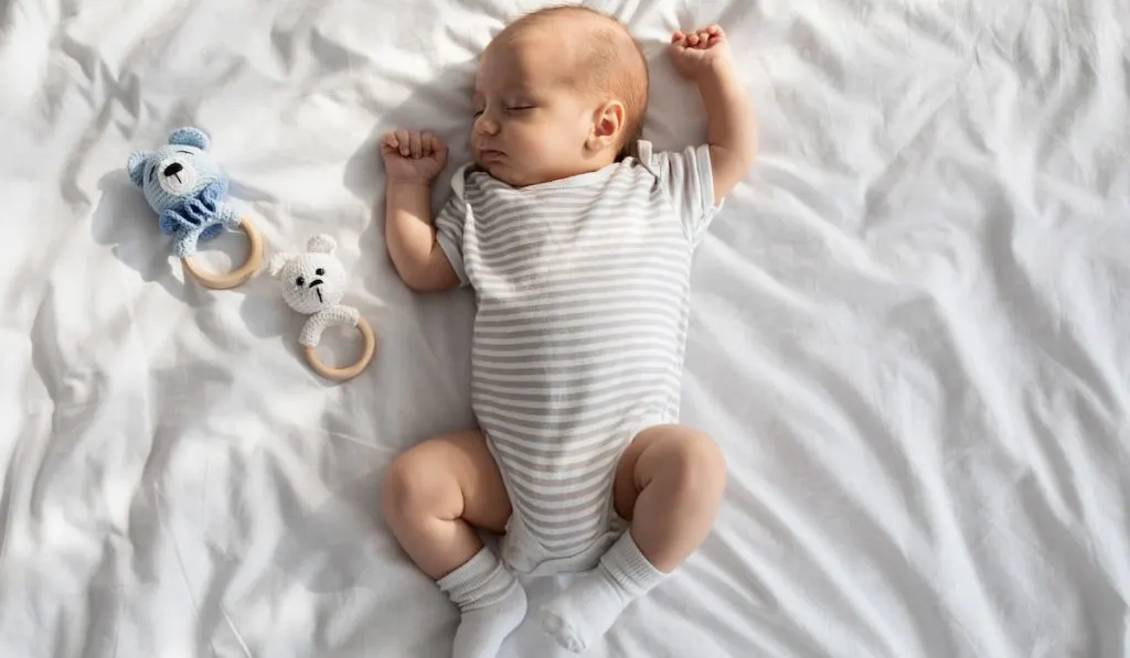 Cute sleeping baby On Bed With Rattle Toys Around 