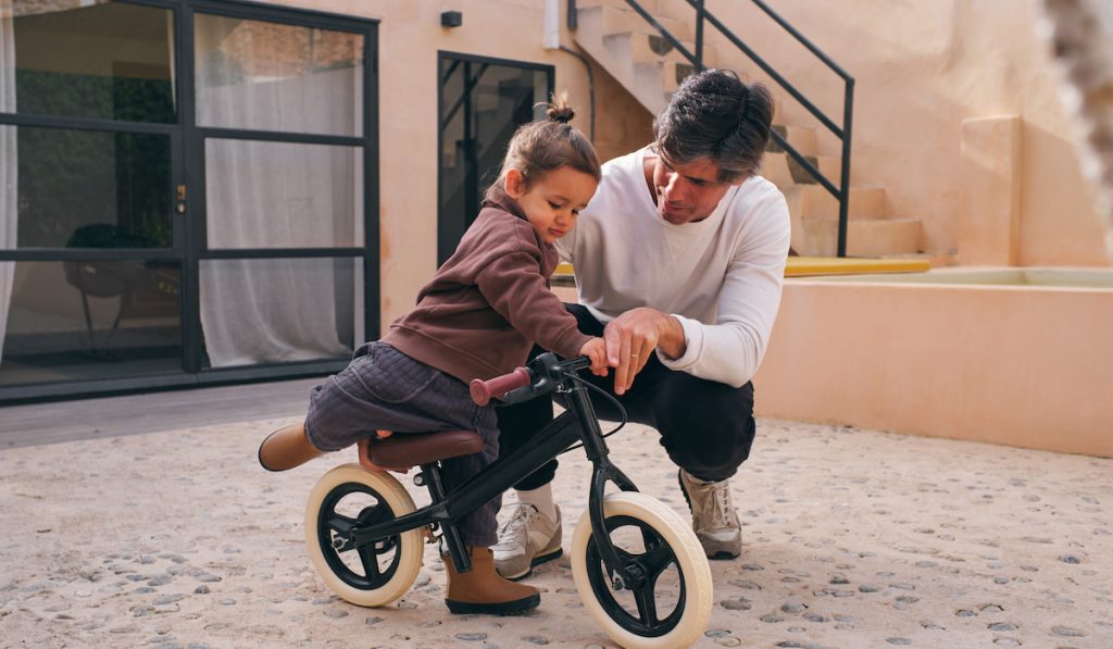 Father interacting with daughter on on how to ride a balance bike in patio 