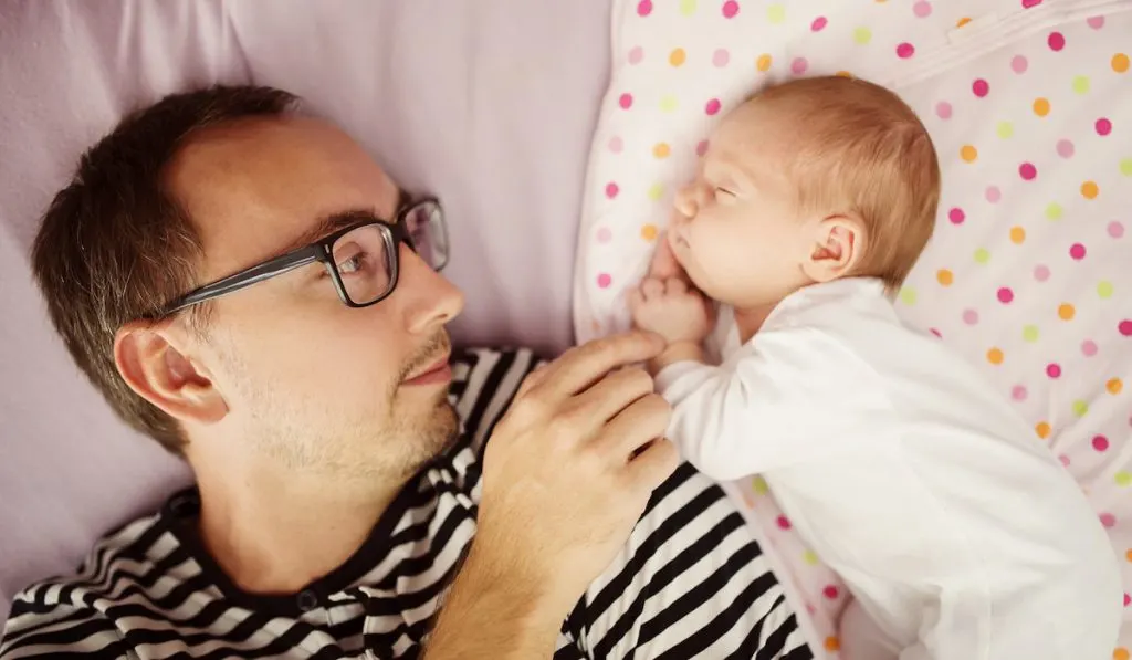 Father with his sleeping newborn baby at home 