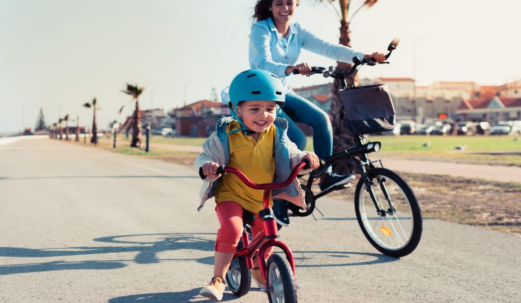 Little kid riding a balance bike with his mother on a bicycle
