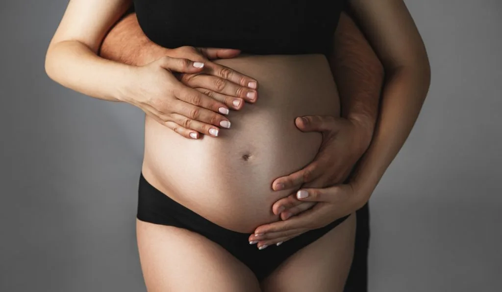 Male and female hands hug a pregnant woman.