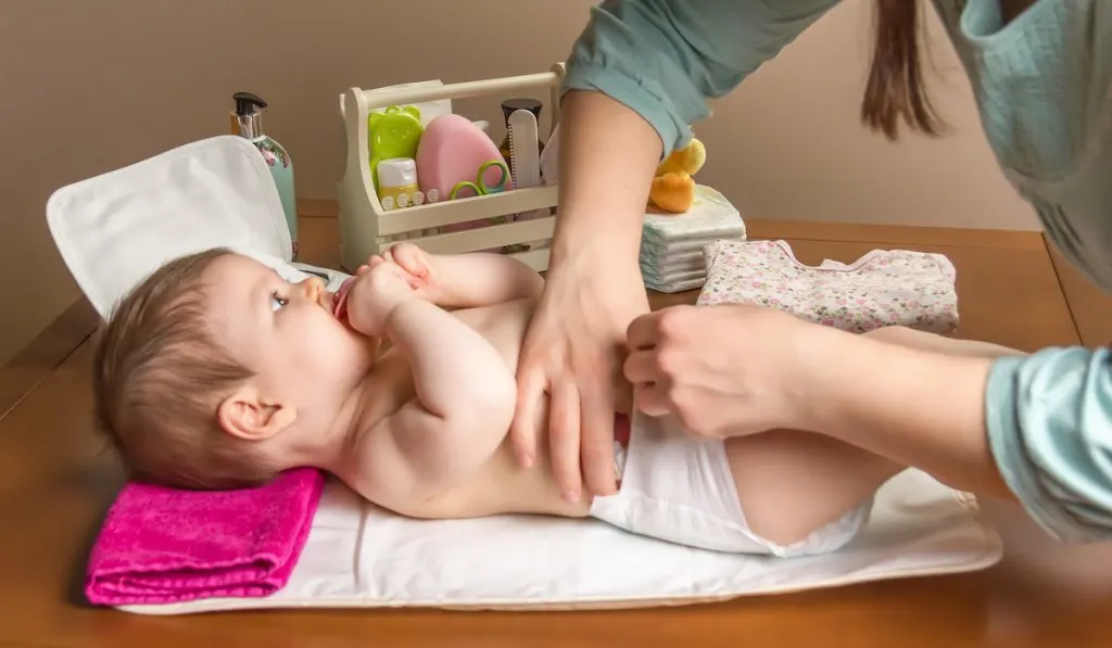 Mother changing diaper of baby and her changing necessities on the side 