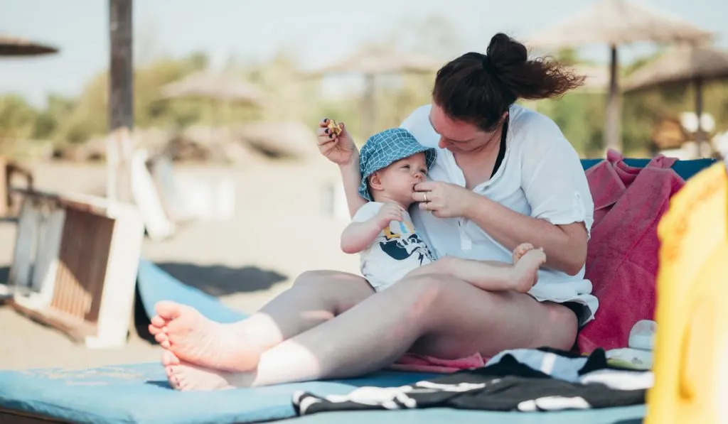 Mother feeding her baby boy with a banana on a beach
