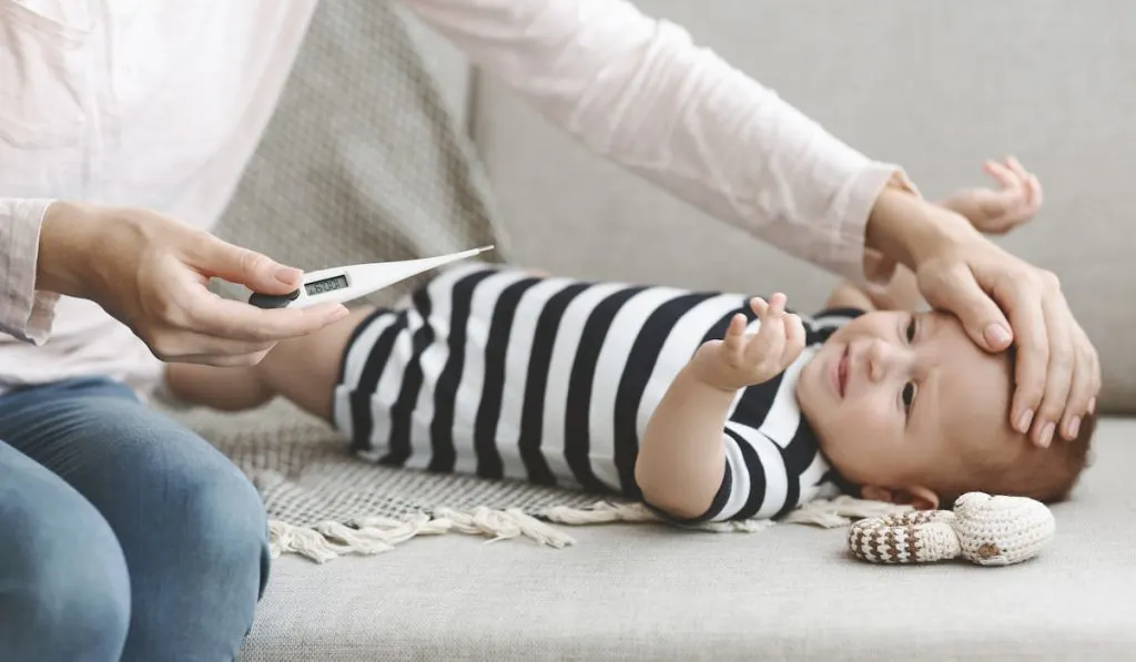 Mother holding thermometer measuring temperature of her sick baby
