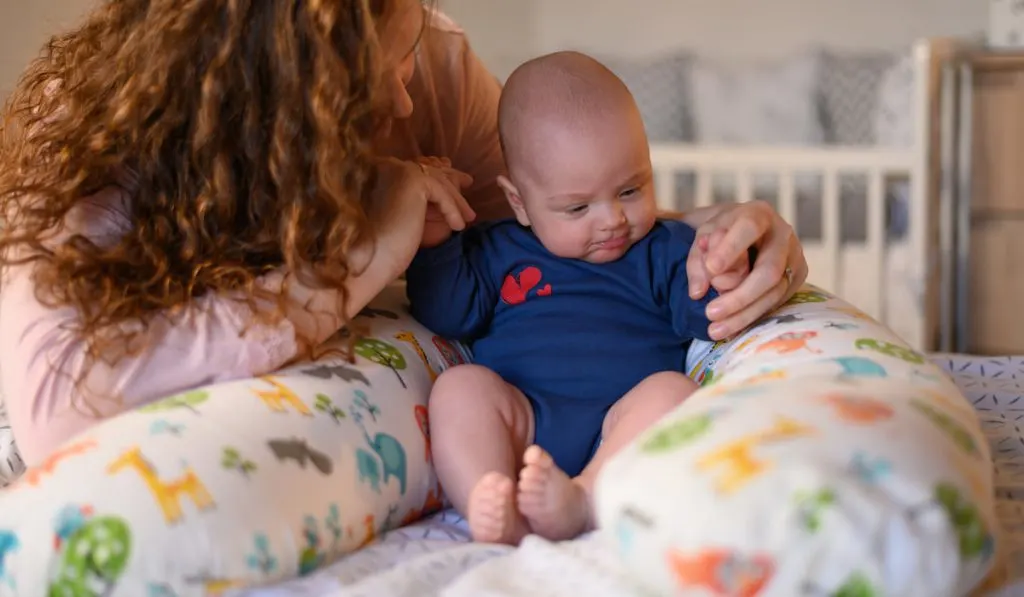 Mother playing with her baby boy while on nursing pillow