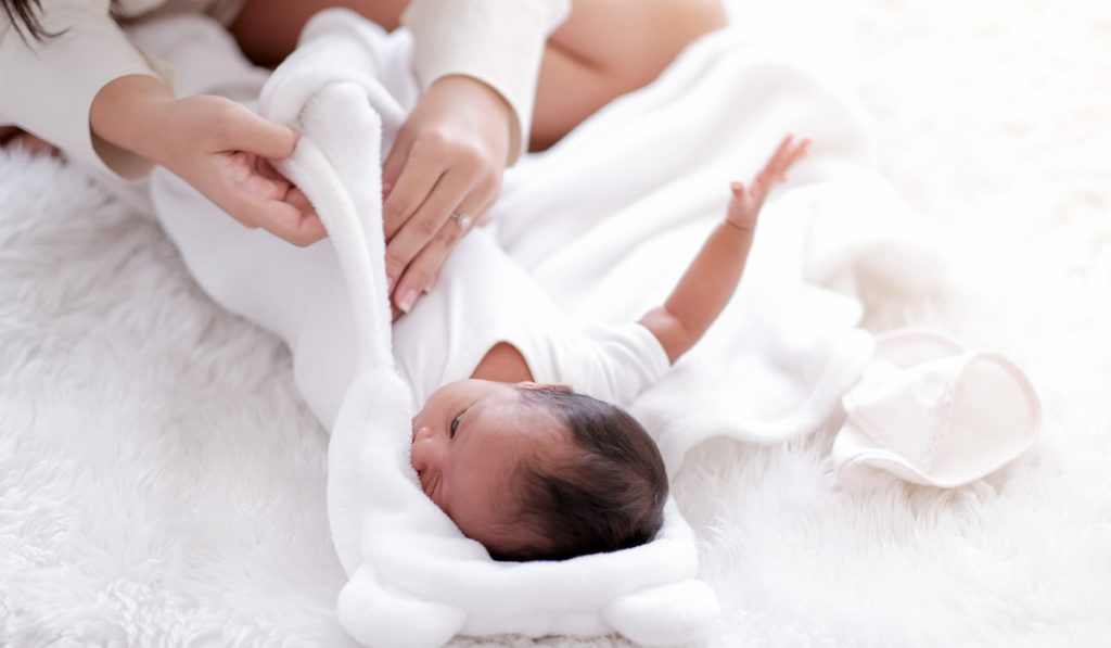 Newborn baby look to mother face and show her hand during swaddling with white cloth