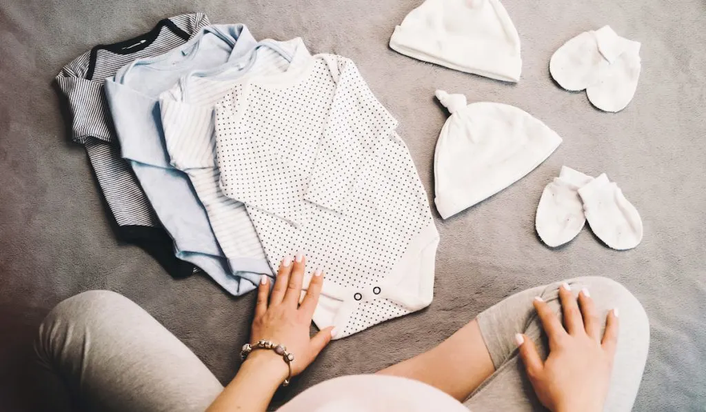 Pregnant Woman sitting with baby clothes neutral colors