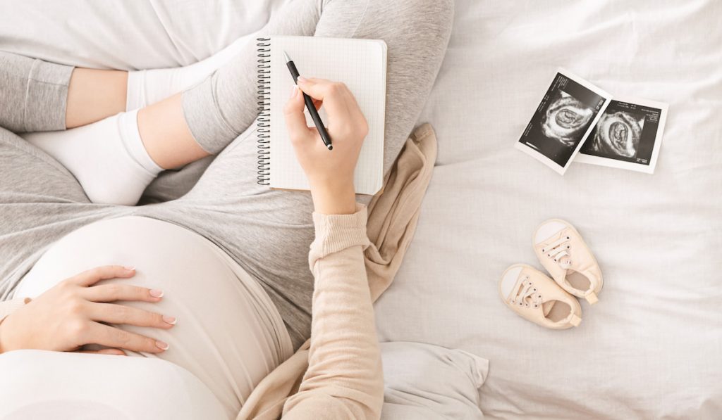 Pregnant woman preparing for labor, sitting on bed with notebook