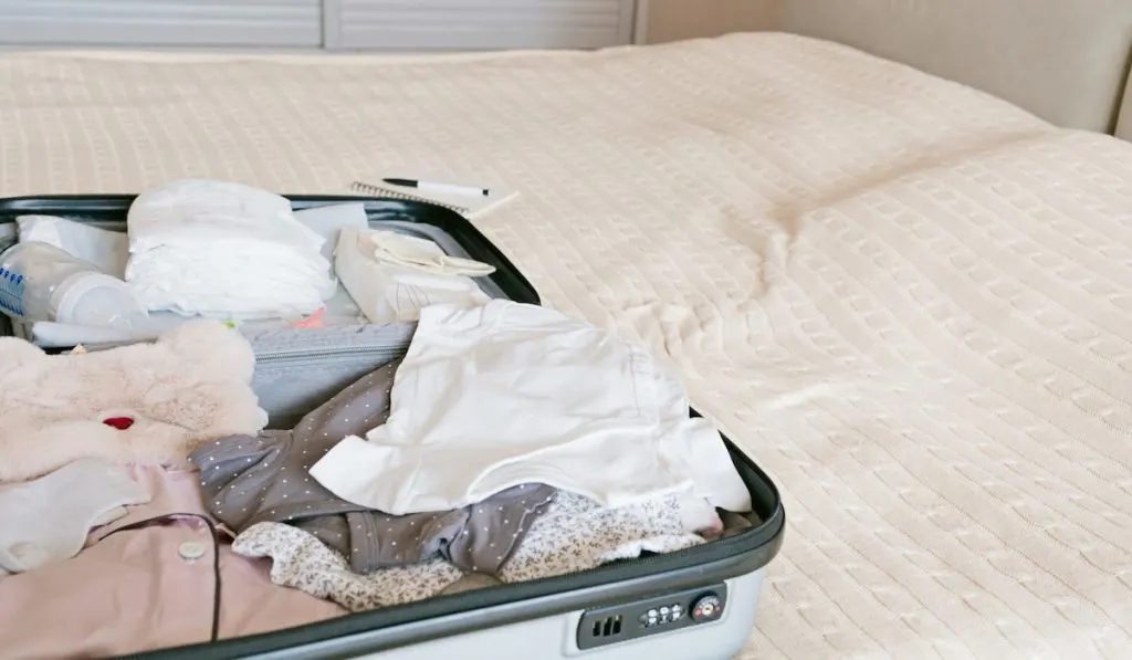 Preparing Suitcase with clothing and newborn baby needs on the bed