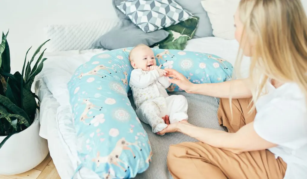 Smiling mother with her baby girl in soft nursing pillow