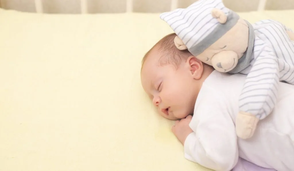 The baby is sleeping in his crib with teddy bear in pajamas