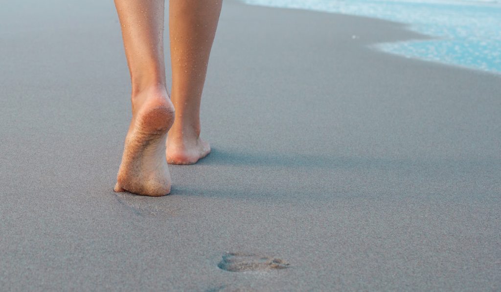 Woman walking on sand beach leaving footprint in the sand
