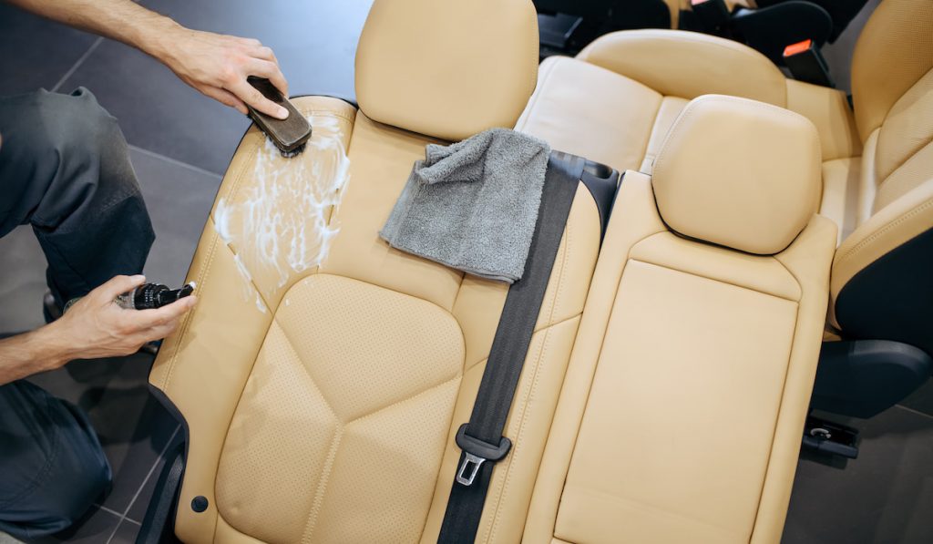 Worker with brush and spray wipes car seat 