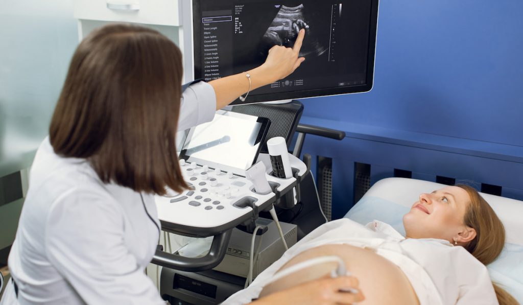 Young excited pregnant woman getting ultrasound in modern clinic
