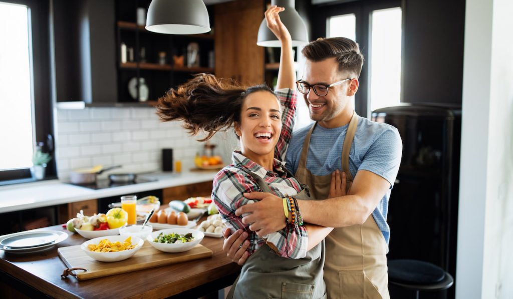 Young happy couple is enjoying and preparing healthy meal in their kitchen 
