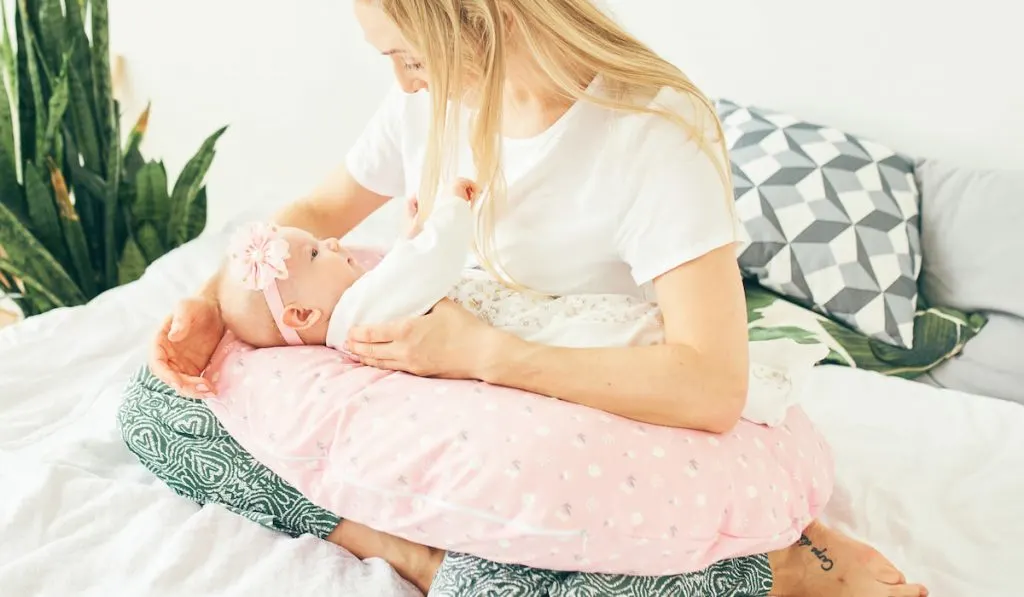 Young mother with baby in bed with boppy pillow 