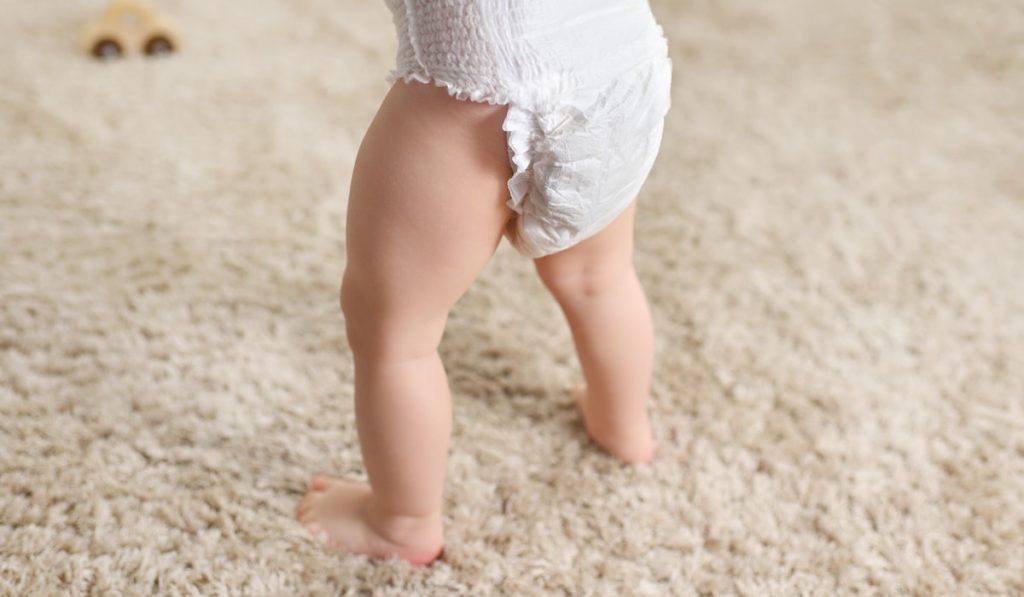 a baby in a disposable diaper on the background of a fluffy carpet.
