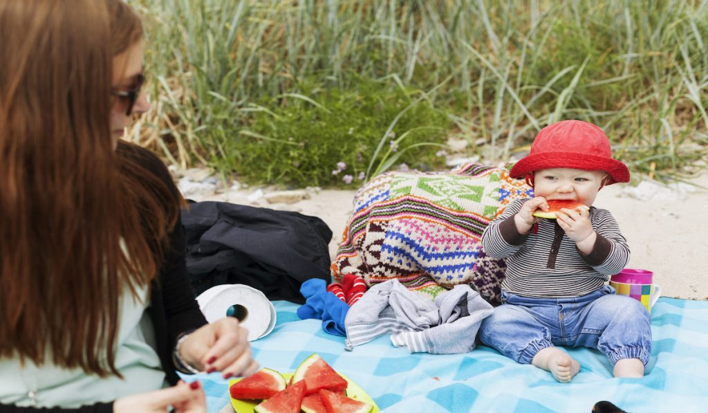 baby boy eating watermelon at the beach with mommy 