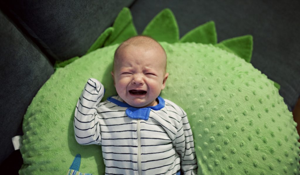 baby crying on a green boppy pillow