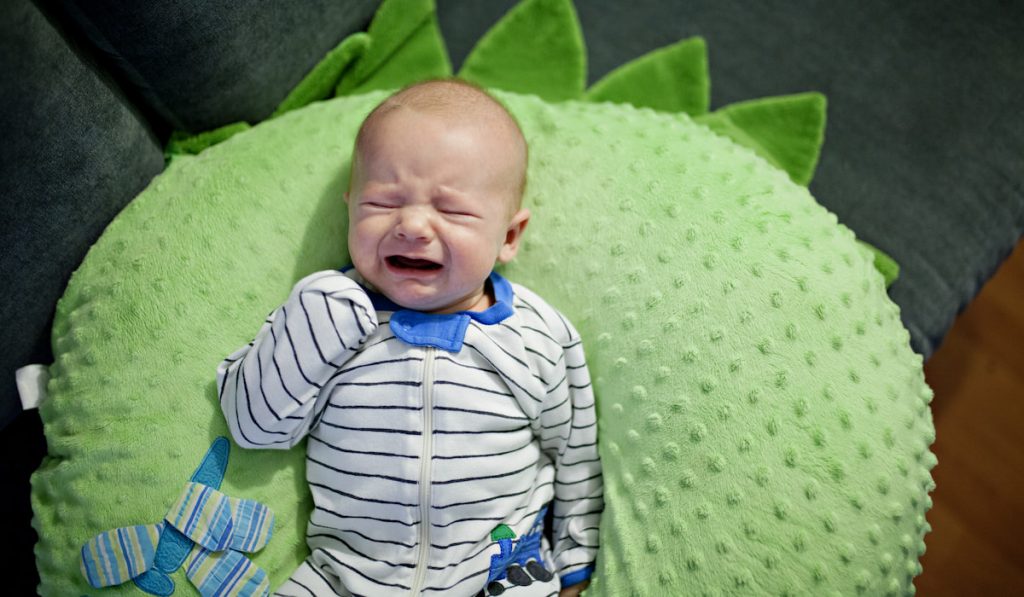 baby crying on a green pillow 