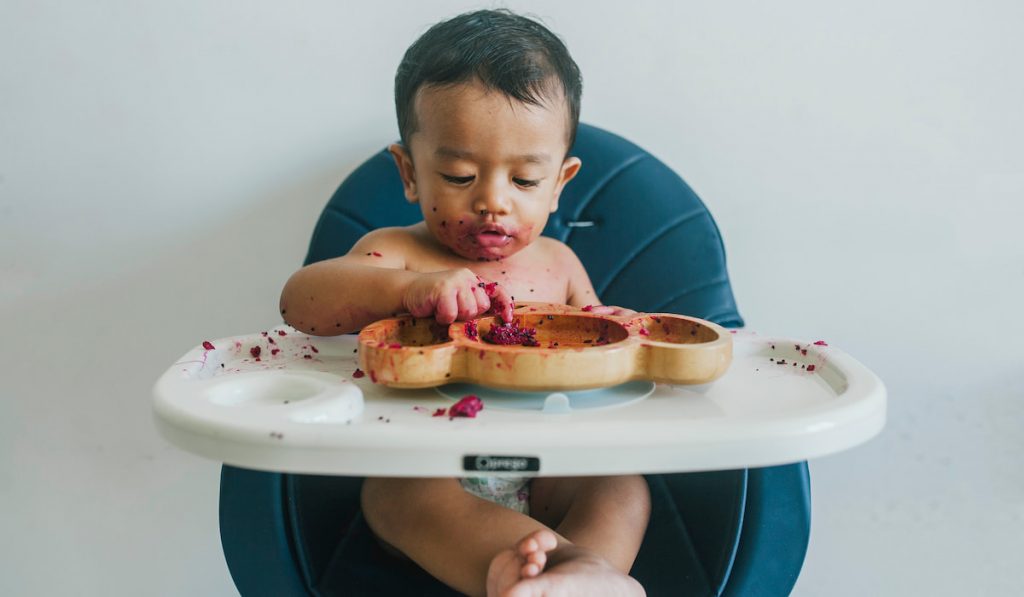 baby picking his fruit on his plate while sitting in high chair 