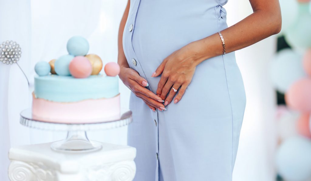 baby shower party pregnant woman standing next to pink and blue cake