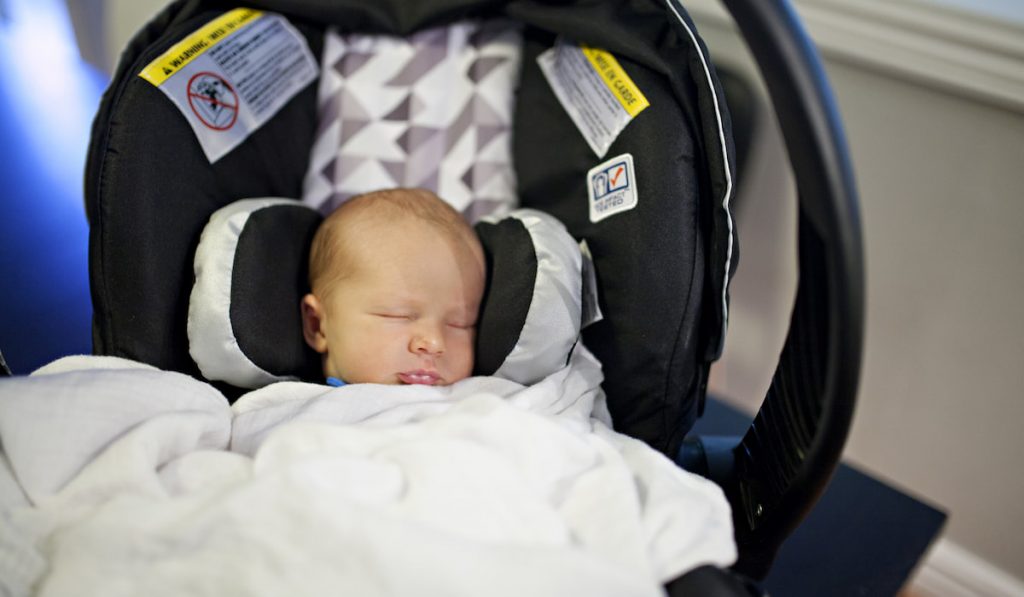 baby sleeping in a carseat with blanket