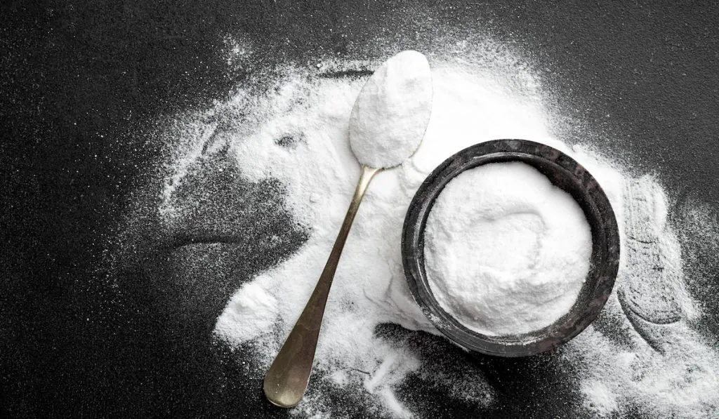 baking soda in black jar and spoon on black background 