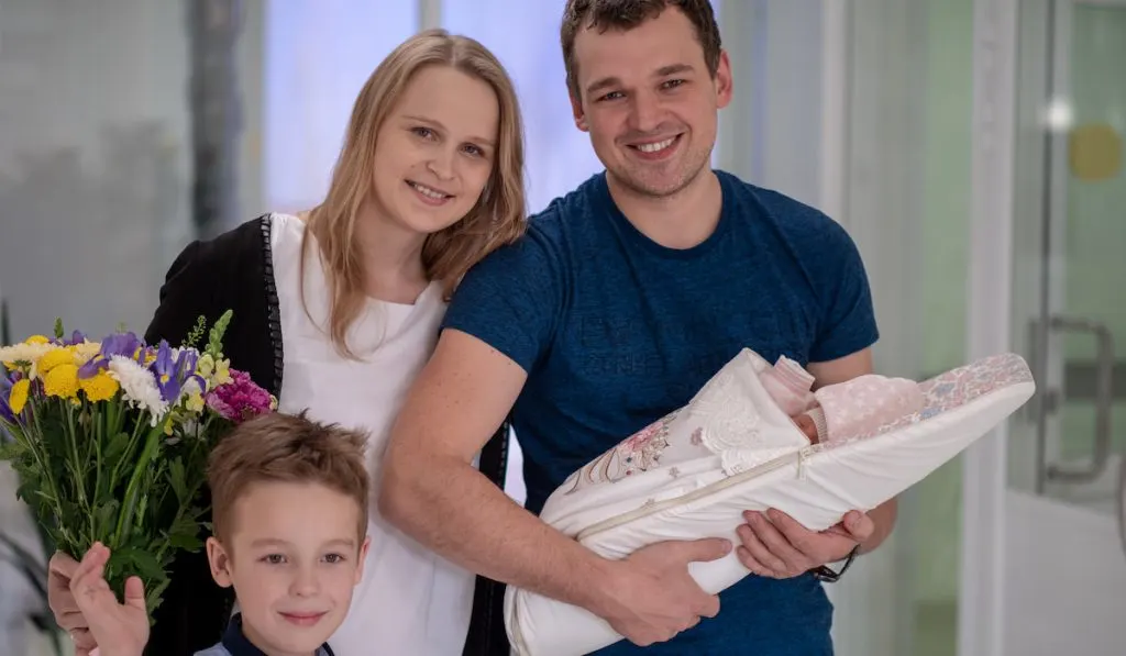 father and son giving flowers to mommy with their newborn baby 