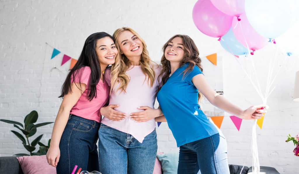 friends and pregnant woman posing with balloons at baby shower party 