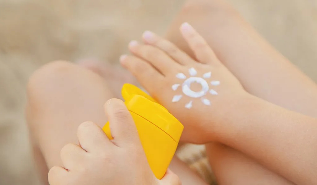 hand of a baby holding sunscreen and sun shape cream on hand