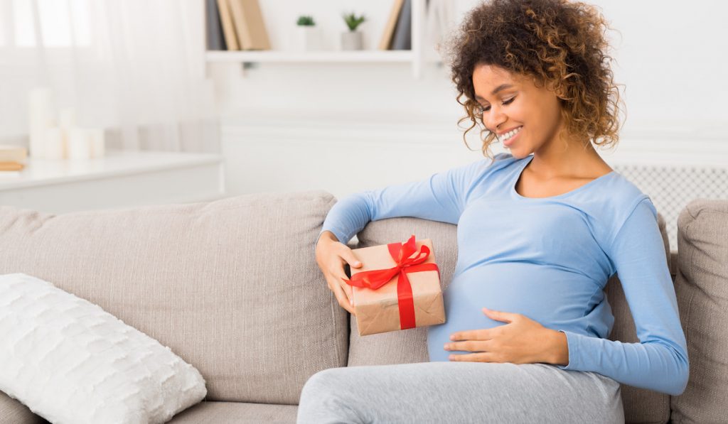 happy pregnant woman with her gift box on the sofa