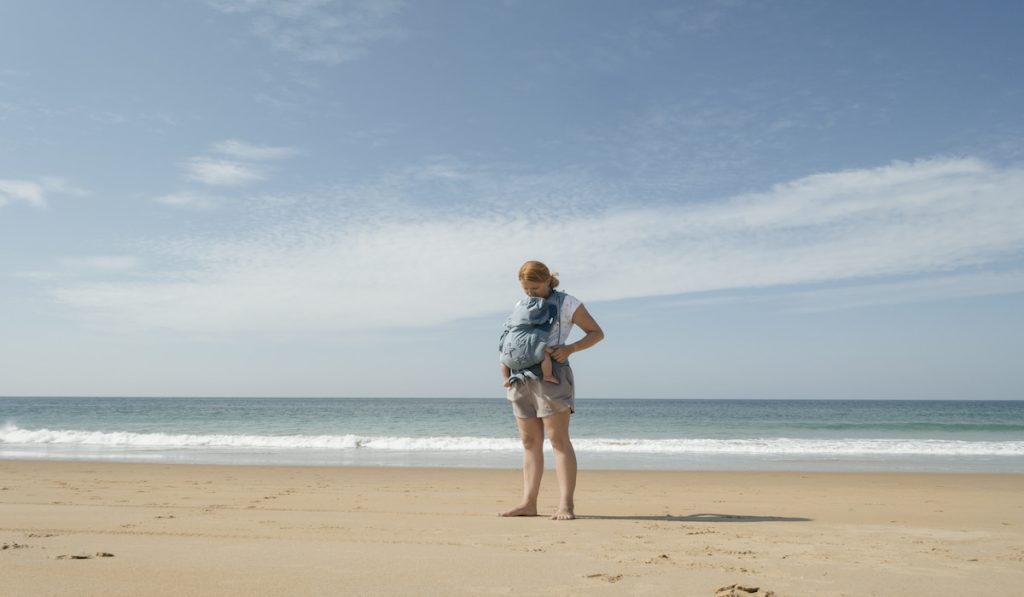 mommy carrying baby sing a baby carrier at the beach