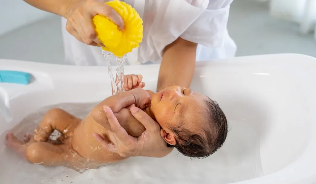 mother bathing newborn baby in white bathtub