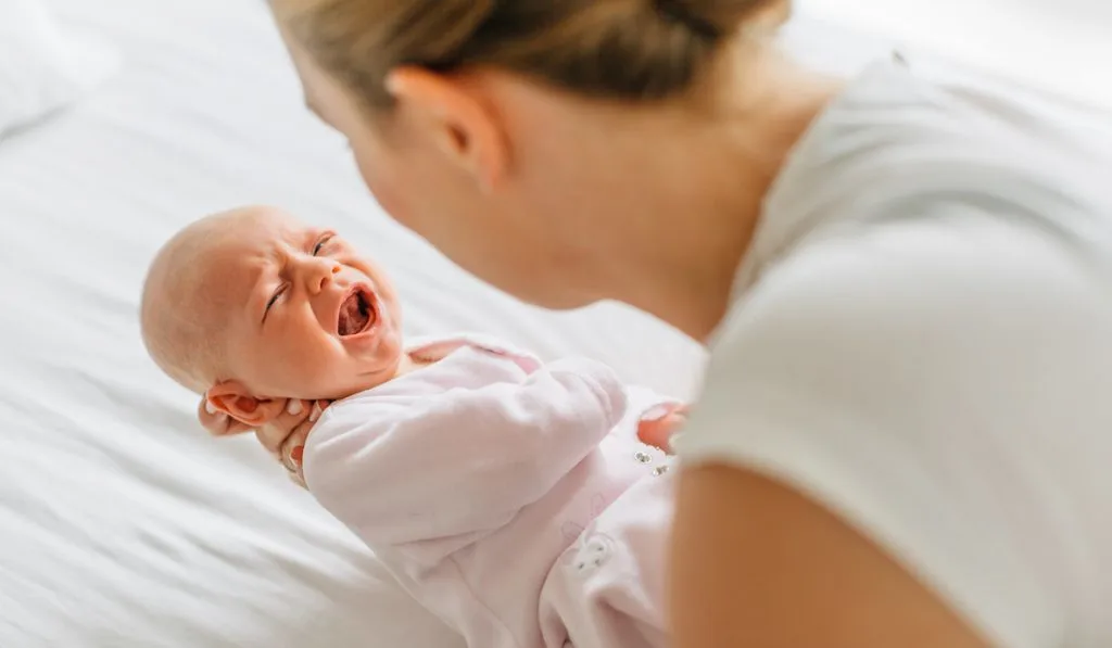 mother cradling crying baby daughter while putting on crib