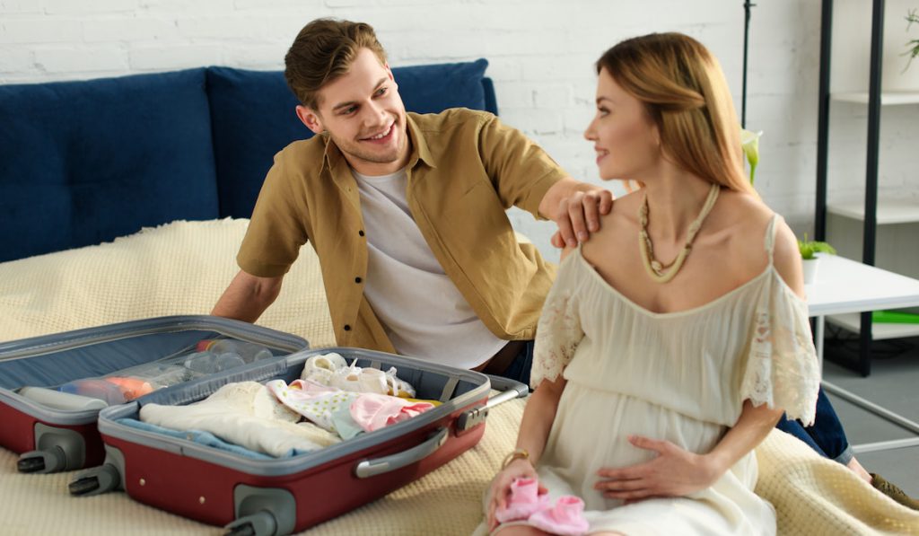 pregnant wife and happy husband packing suitcase for hospital at home