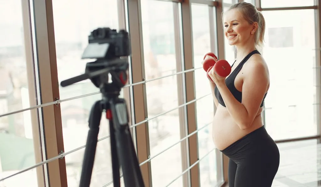 pregnant woman in sporty attire posing for photoshoot while holding dumbells