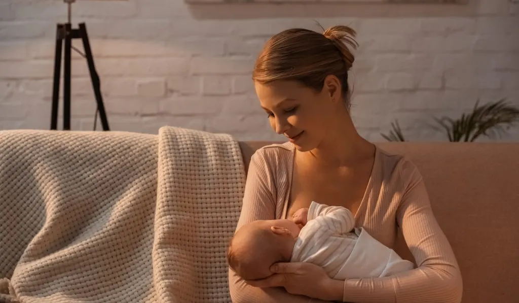 smiling young mother breastfeeding baby at night 