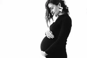 Happy young pregnant woman in stylish black dress holding belly bump and posing
