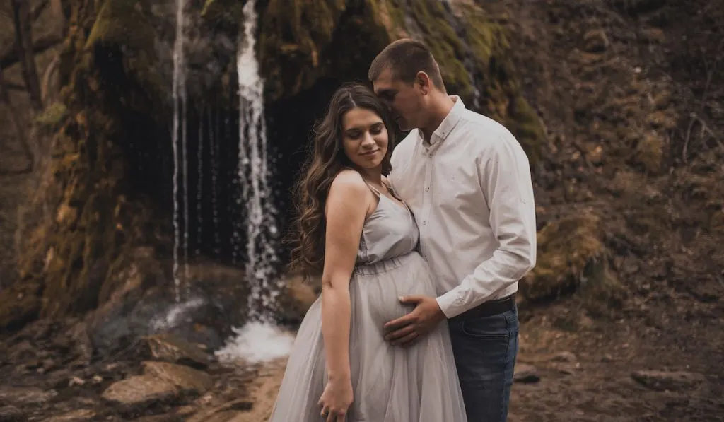 Husband holding his pregnants wife belly posing in nature background 