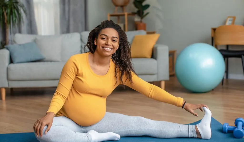Pregnant woman doing exercises and practicing yoga at home wearing leggings