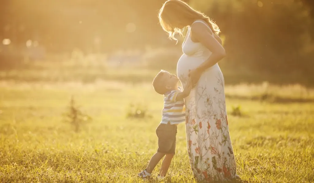 Small boy kissing belly of his pregnant mother outdoors
